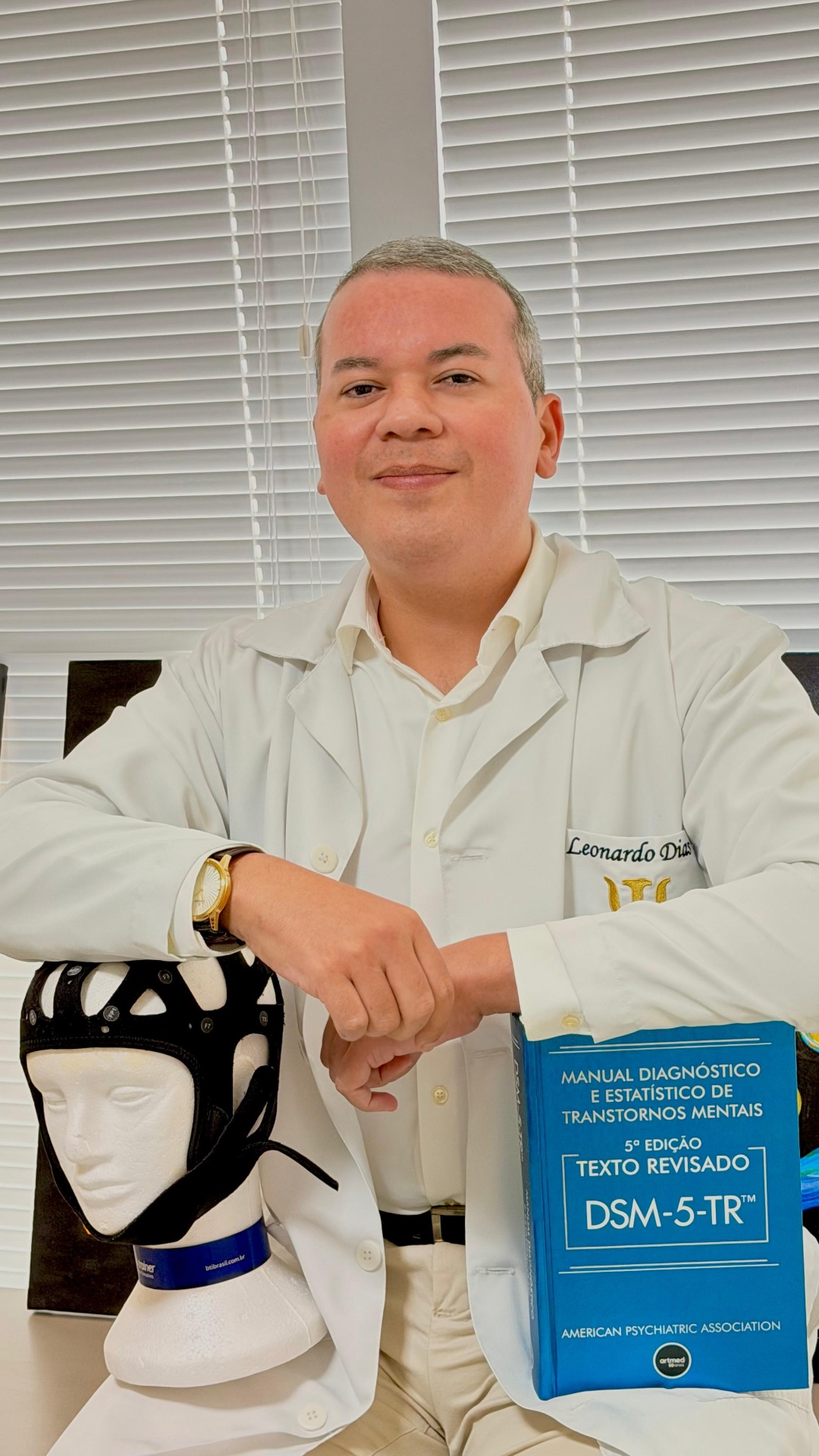 Dr. Leonardo Dias com capacete EEG do Brain-Trainer e DSM-5-TR no consultório